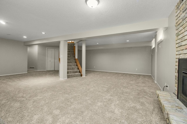 finished basement with visible vents, a textured ceiling, a large fireplace, carpet, and stairs