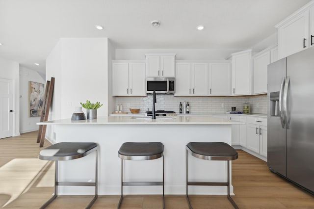 kitchen with light wood finished floors, white cabinets, appliances with stainless steel finishes, and a breakfast bar area