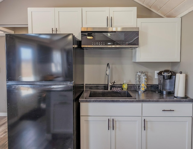 kitchen with dark countertops, white cabinets, freestanding refrigerator, and a sink