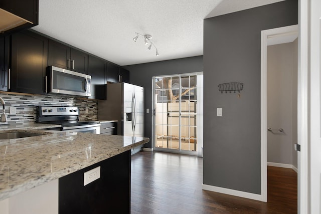 kitchen featuring dark wood-style floors, a sink, decorative backsplash, appliances with stainless steel finishes, and a textured ceiling