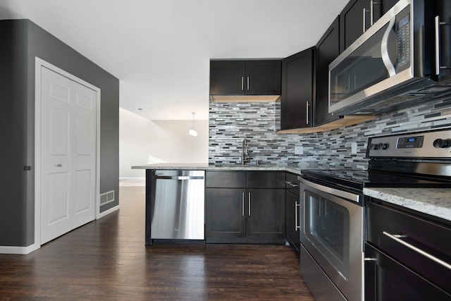 kitchen featuring tasteful backsplash, light stone countertops, dark wood finished floors, stainless steel appliances, and a sink