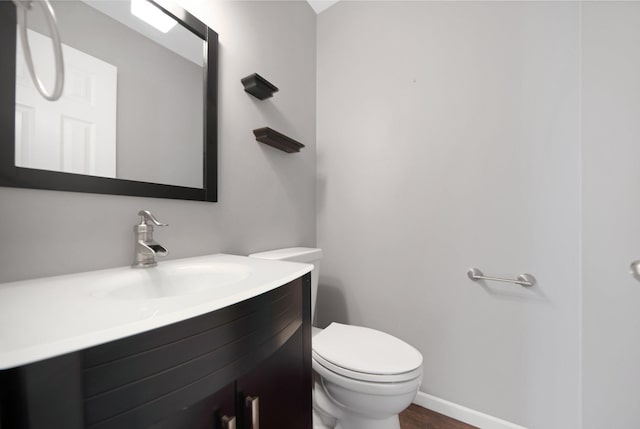 bathroom with toilet, vanity, baseboards, and wood finished floors