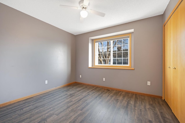 empty room with a ceiling fan, visible vents, baseboards, and dark wood-style flooring