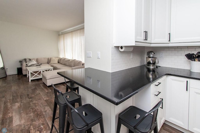 kitchen featuring dark wood-type flooring, white cabinetry, dark countertops, a kitchen breakfast bar, and open floor plan