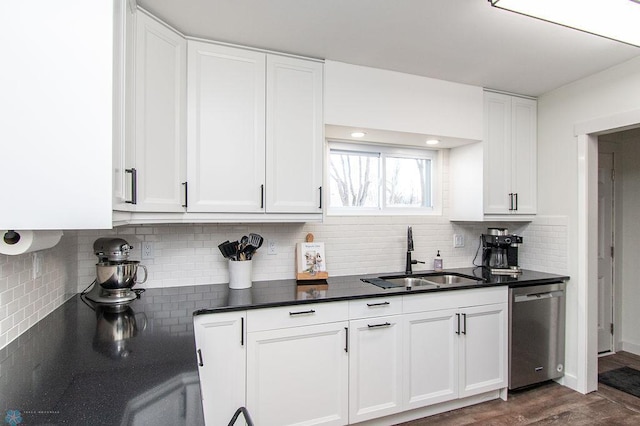 kitchen with dark countertops, tasteful backsplash, dishwasher, white cabinets, and a sink