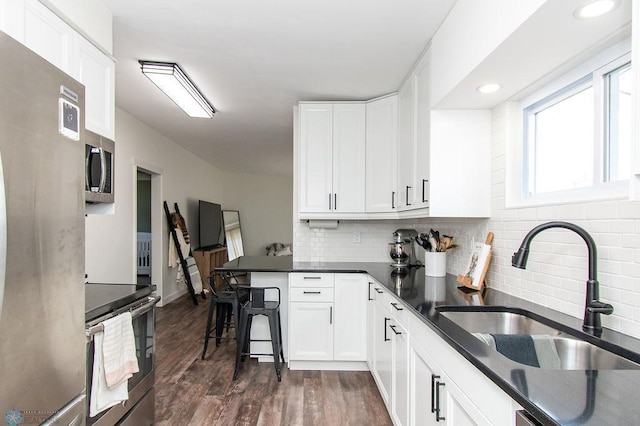 kitchen featuring dark wood-type flooring, a sink, appliances with stainless steel finishes, white cabinets, and decorative backsplash