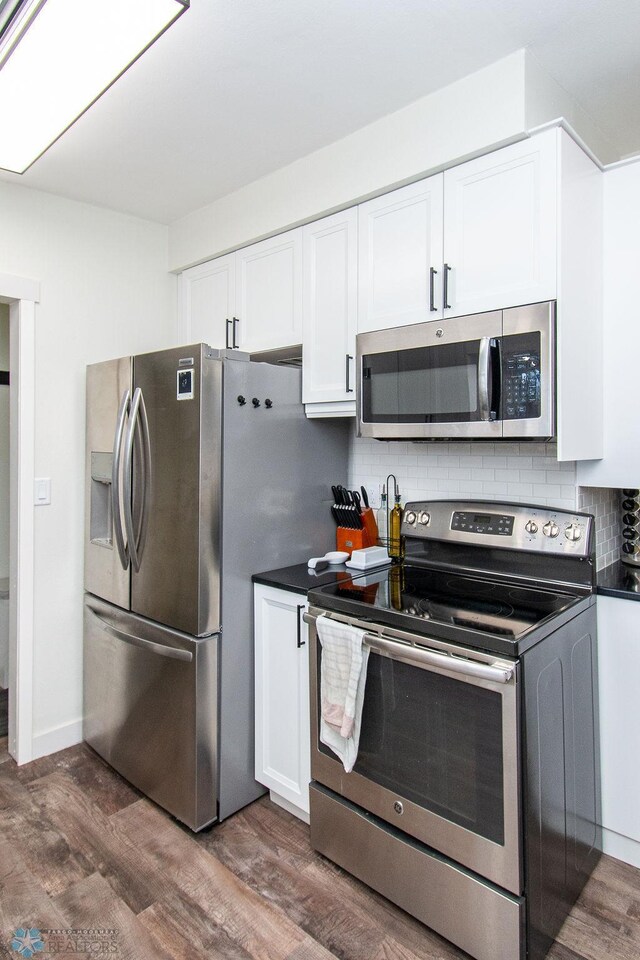 kitchen with backsplash, dark countertops, stainless steel appliances, white cabinets, and dark wood-style flooring