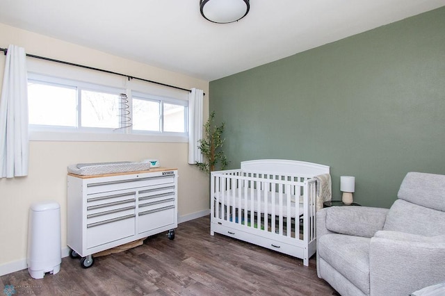 bedroom featuring a nursery area, wood finished floors, and baseboards