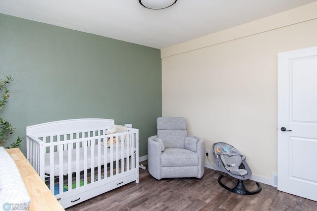 bedroom featuring baseboards, a nursery area, and wood finished floors