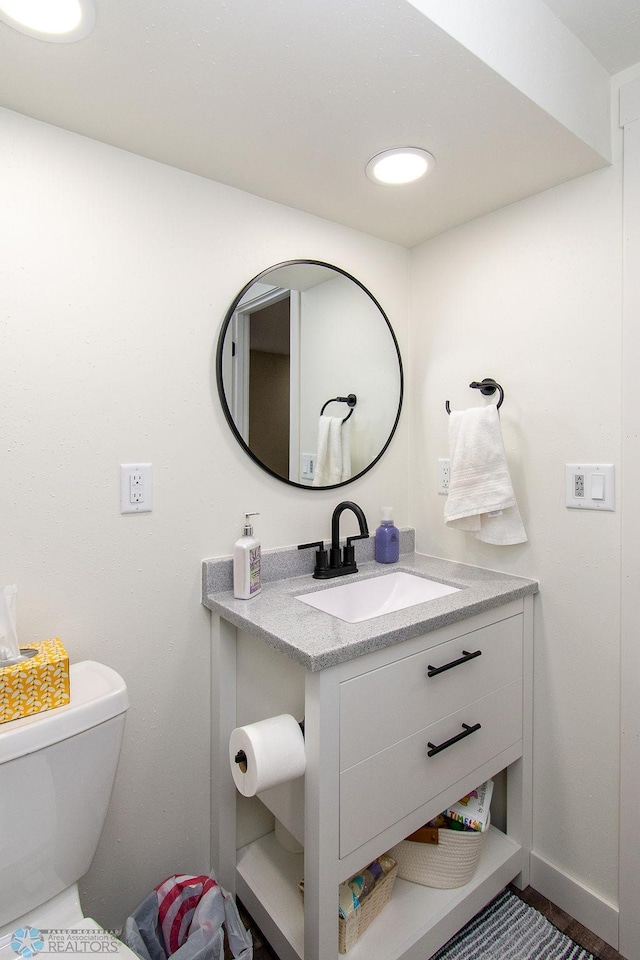 half bathroom with vanity, toilet, recessed lighting, and baseboards