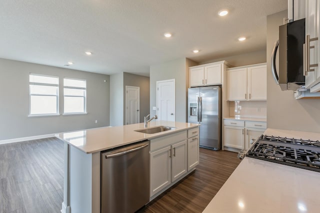 kitchen featuring dark wood finished floors, an island with sink, a sink, light countertops, and appliances with stainless steel finishes