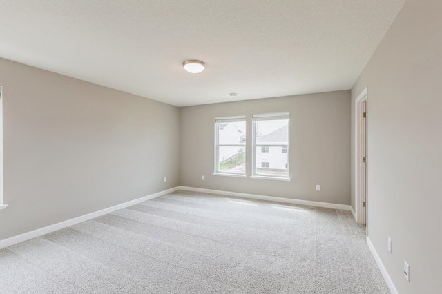 empty room featuring light colored carpet, a textured ceiling, and baseboards