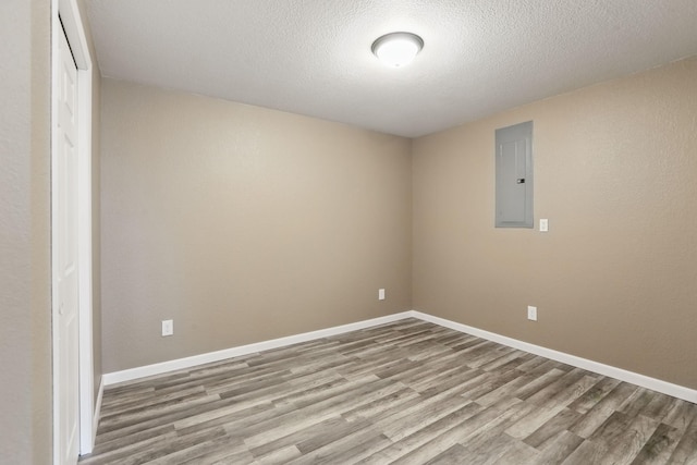 spare room with electric panel, a textured ceiling, baseboards, and wood finished floors