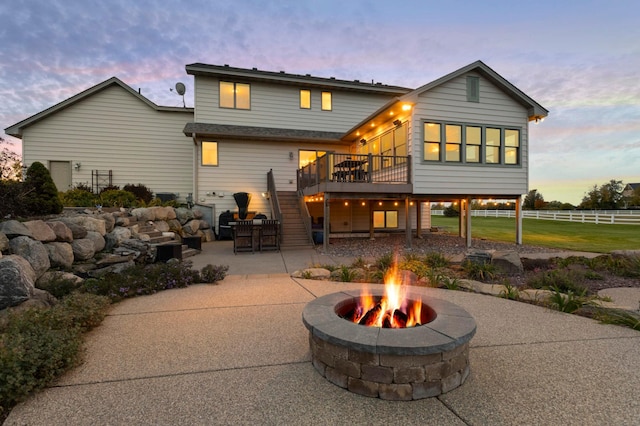 back of property at dusk with fence, stairway, an outdoor fire pit, a wooden deck, and a patio area