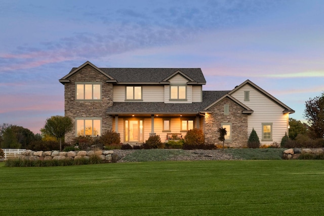 traditional-style home featuring a lawn, stone siding, and roof with shingles