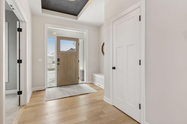 foyer entrance with light wood-type flooring, a raised ceiling, and baseboards