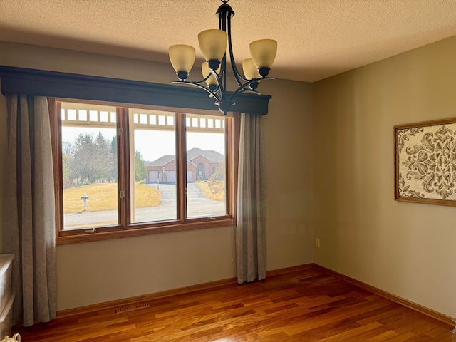 spare room featuring visible vents, a textured ceiling, wood finished floors, baseboards, and a chandelier