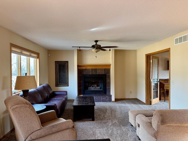 living room featuring visible vents, baseboards, a tiled fireplace, carpet flooring, and a textured ceiling