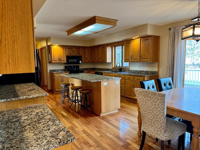 kitchen featuring light wood finished floors, black appliances, a kitchen breakfast bar, brown cabinets, and a center island