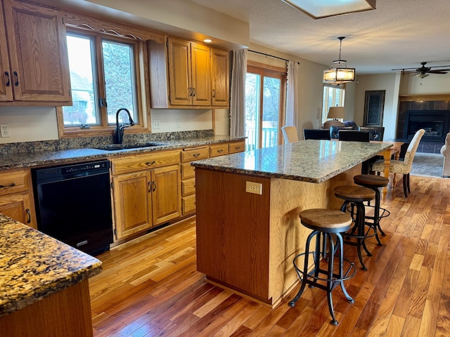 kitchen with a center island, light wood-type flooring, black dishwasher, a kitchen breakfast bar, and a sink