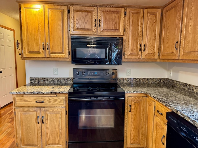 kitchen with stone countertops, brown cabinets, black appliances, and light wood finished floors