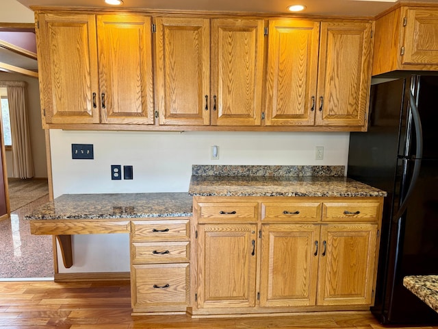 kitchen with dark stone counters, light wood-type flooring, freestanding refrigerator, and brown cabinets