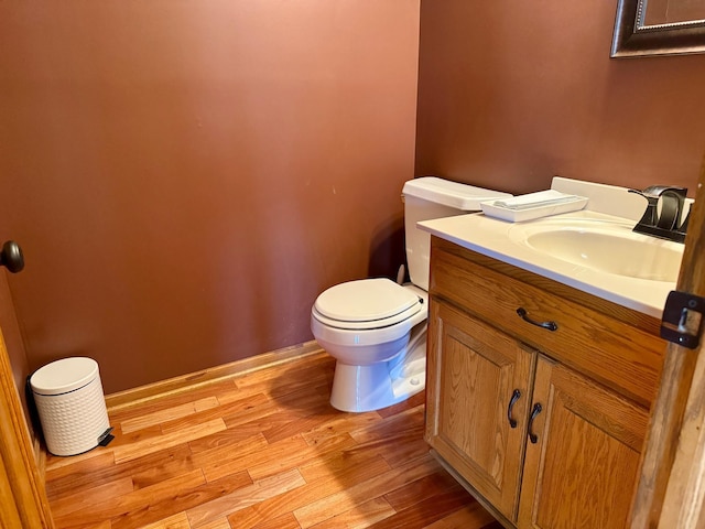 half bath featuring vanity, toilet, wood finished floors, and baseboards