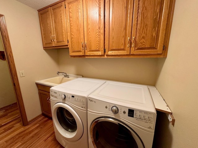 clothes washing area with baseboards, washer and clothes dryer, light wood-type flooring, cabinet space, and a sink