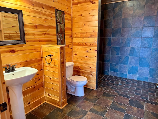 bathroom with a sink, wooden walls, toilet, and tiled shower