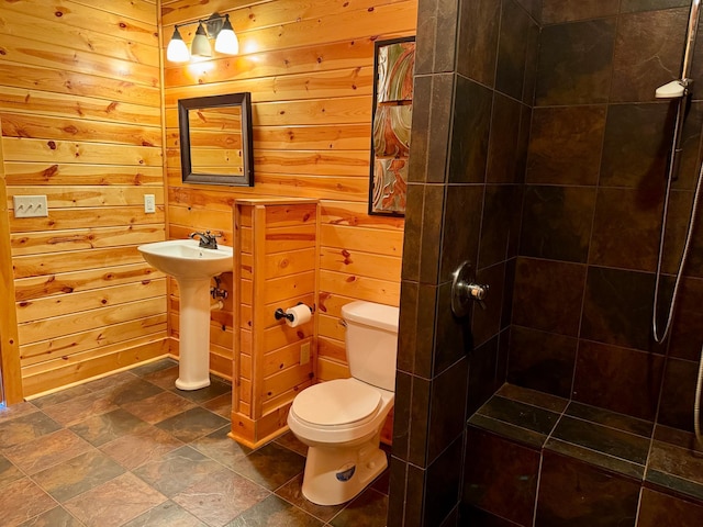 full bath featuring stone finish flooring, tiled shower, toilet, and wooden walls