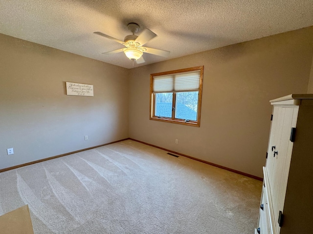 empty room featuring a textured ceiling, light colored carpet, baseboards, and ceiling fan