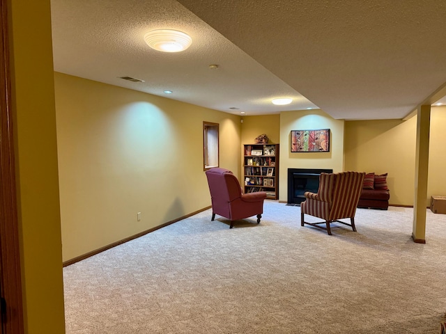 sitting room with visible vents, baseboards, carpet flooring, a glass covered fireplace, and a textured ceiling