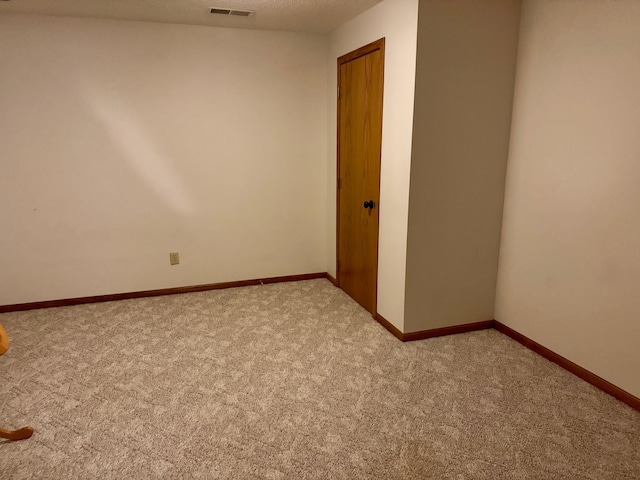 unfurnished room featuring visible vents, light colored carpet, a textured ceiling, and baseboards