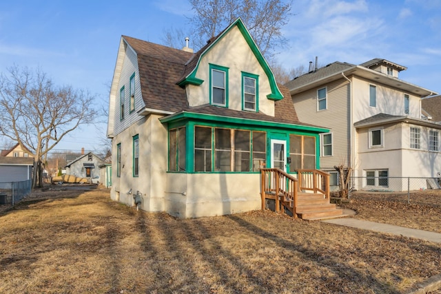 view of front of home with a gambrel roof, fence, roof with shingles, and a sunroom