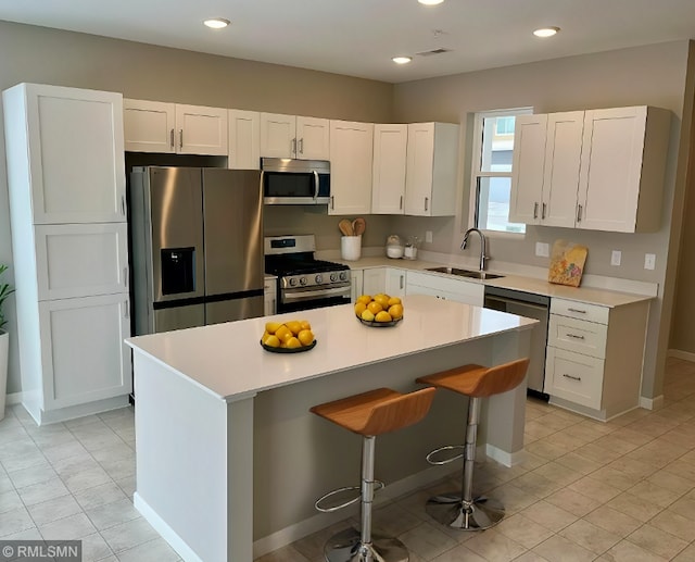 kitchen with a sink, stainless steel appliances, a kitchen island, and white cabinets