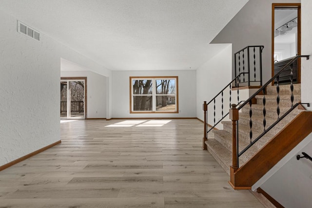 interior space featuring visible vents, baseboards, a textured wall, wood finished floors, and a textured ceiling