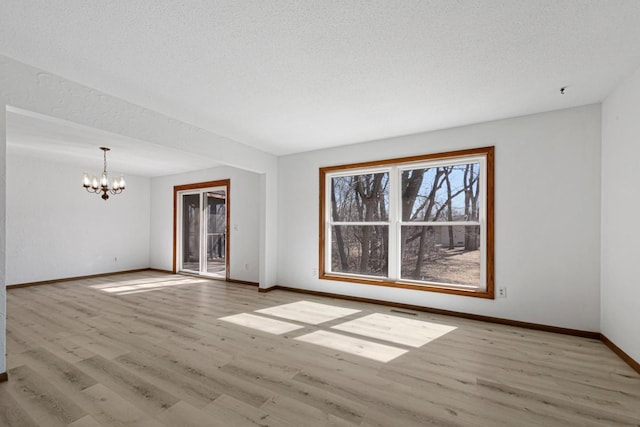 spare room with baseboards, a notable chandelier, wood finished floors, and a textured ceiling