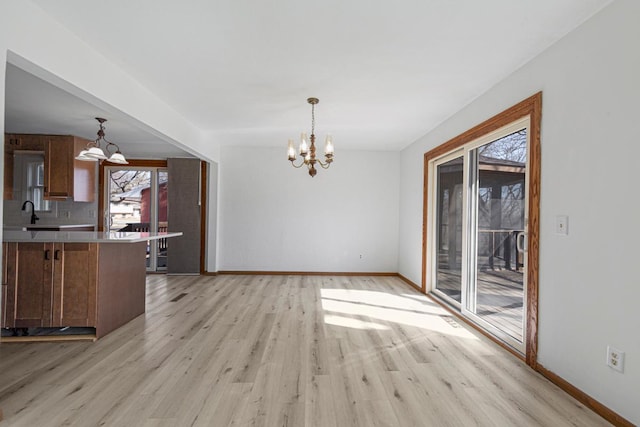 unfurnished dining area with a notable chandelier, light wood-style floors, and baseboards