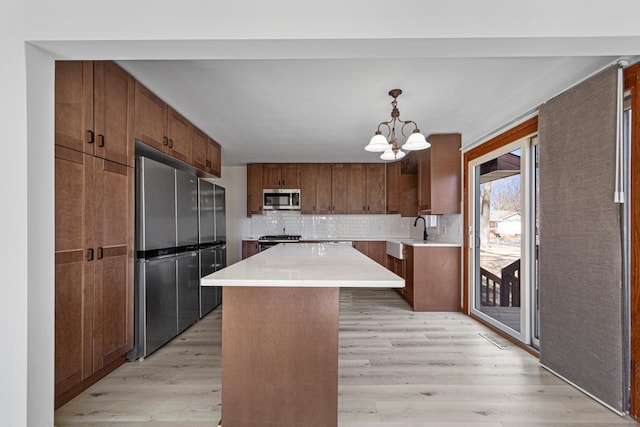 kitchen with a center island, light countertops, decorative backsplash, light wood-style flooring, and appliances with stainless steel finishes