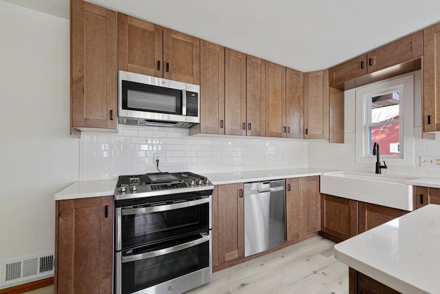 kitchen featuring visible vents, backsplash, brown cabinetry, stainless steel appliances, and a sink