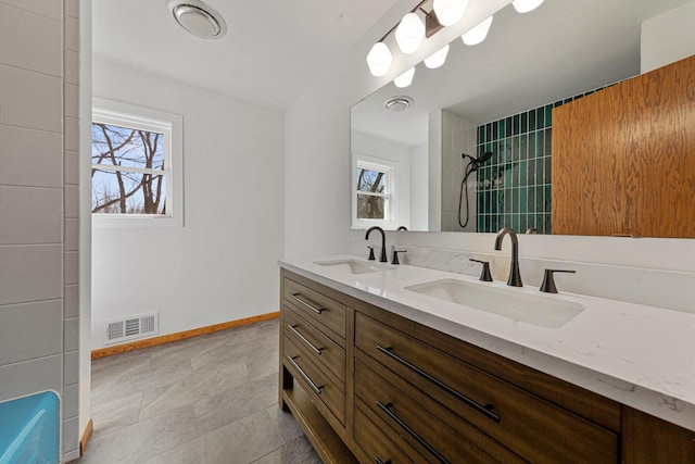 bathroom featuring a tile shower, visible vents, baseboards, and a sink