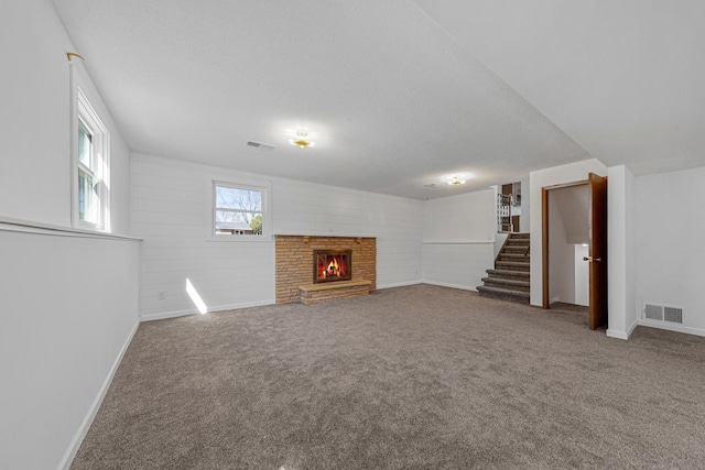 below grade area with stairway, a brick fireplace, visible vents, and carpet floors