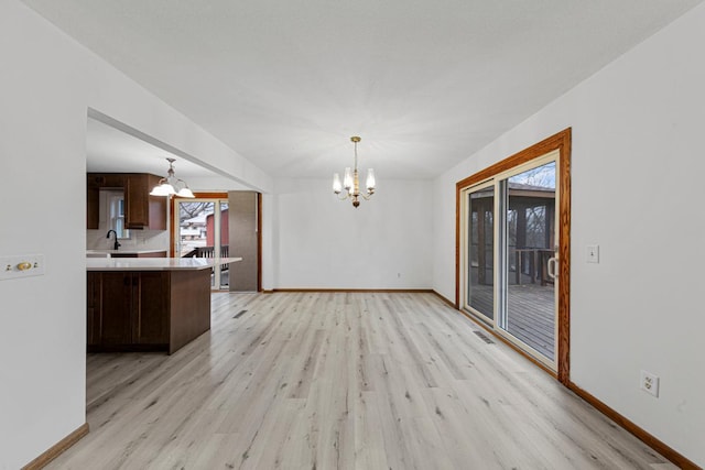 interior space featuring light wood-style flooring, a notable chandelier, and baseboards