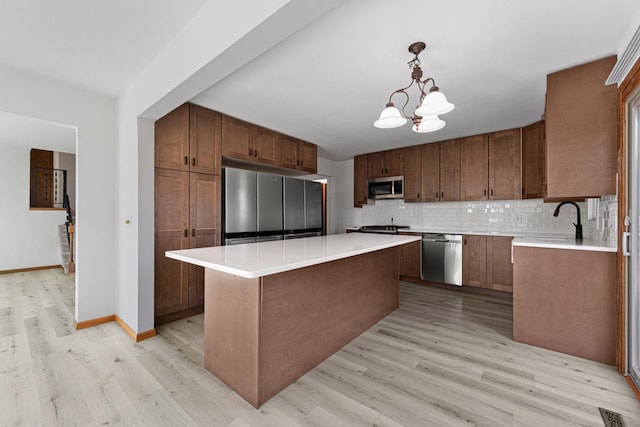 kitchen with tasteful backsplash, appliances with stainless steel finishes, a center island, and light wood-style floors