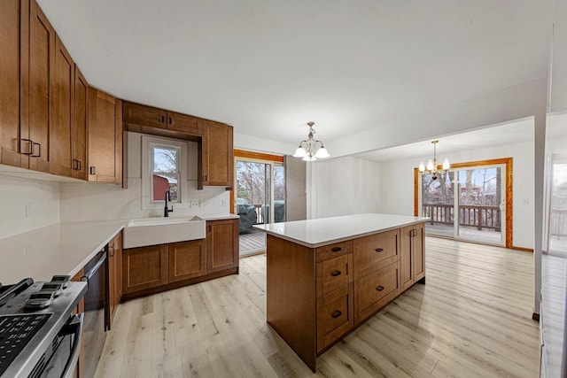 kitchen with brown cabinetry, a sink, light wood-style floors, appliances with stainless steel finishes, and a notable chandelier