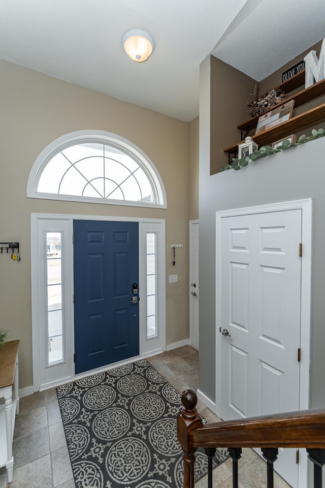 entryway with light tile patterned flooring, baseboards, a wealth of natural light, and a towering ceiling