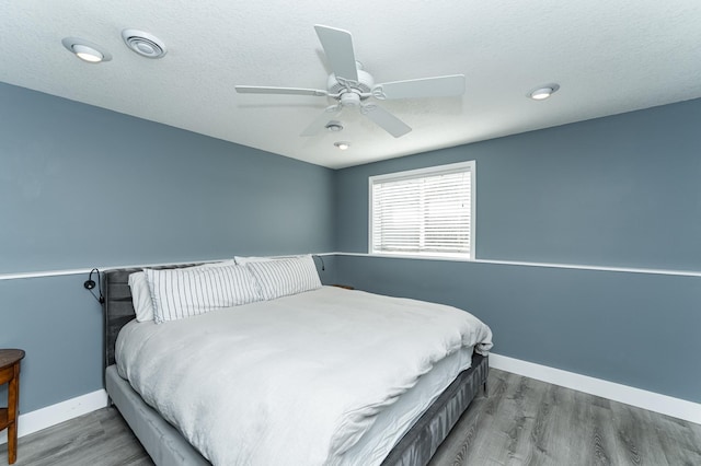 bedroom with visible vents, a textured ceiling, baseboards, and wood finished floors