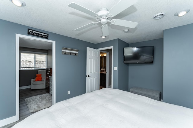 bedroom with visible vents, a textured ceiling, wood finished floors, baseboards, and ceiling fan