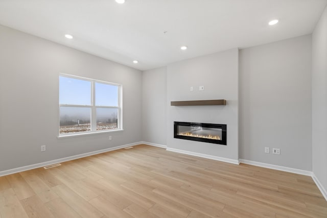 unfurnished living room with light wood finished floors, a glass covered fireplace, recessed lighting, and baseboards