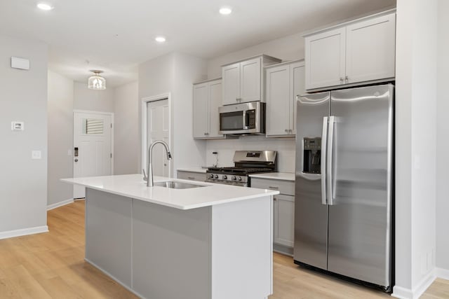 kitchen featuring a kitchen island with sink, appliances with stainless steel finishes, light wood-type flooring, and a sink